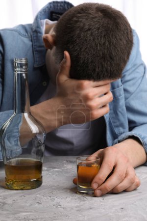 Adicción al alcohol. Hombre con whisky en mesa texturizada gris