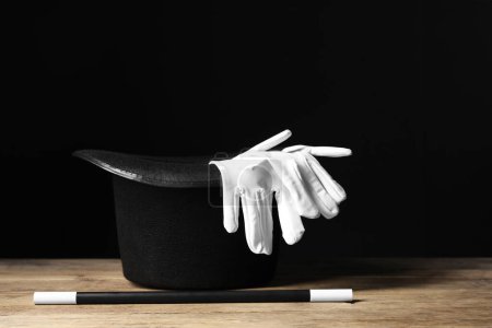 Sombrero de mago, guantes y varita sobre mesa de madera sobre fondo negro
