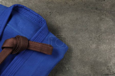 Brown karate belt and blue kimono on gray textured background, top view. Space for text