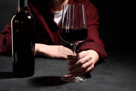 Alkoholsucht. Frau mit Rotwein am dunkel strukturierten Tisch, selektiver Fokus