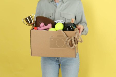Frau hält Schachtel mit unerwünschten Dingen auf gelbem Hintergrund, Nahaufnahme