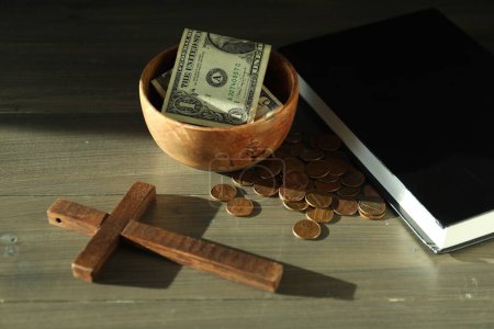 Donate and give concept. Bowl with coins, dollar banknotes, cross and Bible on wooden table