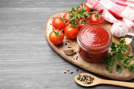 Photo for Tasty ketchup, fresh tomatoes, parsley and spices on grey wooden table, space for text - Royalty Free Image