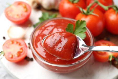 Photo for Taking delicious tomato ketchup with spoon from bowl at light table, closeup - Royalty Free Image