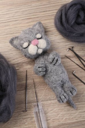 Felted cat, wool and tools on wooden table, flat lay