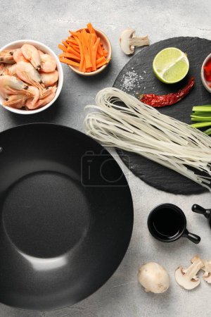 Téléchargez les photos : Composition plate avec wok noir, épices et produits sur table texturée grise - en image libre de droit