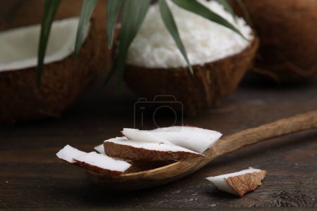 Kokosnussstücke, Löffel und Nuss auf Holztisch, Nahaufnahme