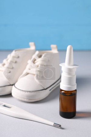Photo for Thermometer, nasal spray and child`s sneakers on grey table, closeup - Royalty Free Image