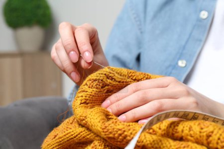 Woman sewing sweater with needle at home, closeup