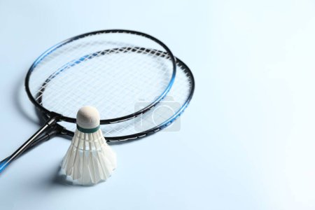 Photo for Feather badminton shuttlecock and rackets on light blue background, closeup. Space for text - Royalty Free Image