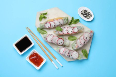 Delicious spring rolls served on light blue background, flat lay