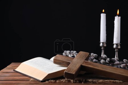 Bougies d'église allumées, croix, Bible et branches de saule sur une table en bois