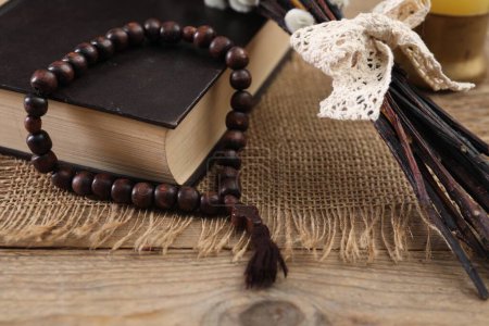 Rosary beads, Bible and willow branches on wooden table, closeup