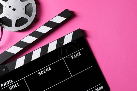 Clapperboard and film reel on pink background, flat lay. Space for text