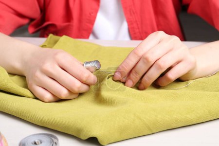 Woman with sewing needle and thread embroidering on cloth at white table, closeup