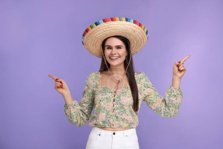 Mujer joven en sombrero mexicano mostrando algo sobre fondo violeta