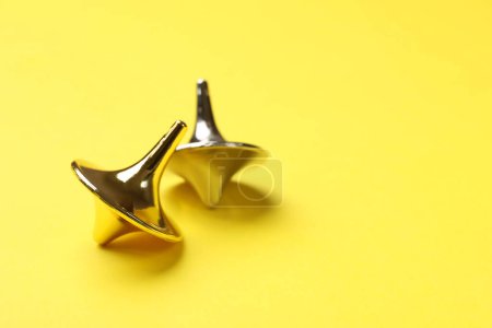 Golden and silver spinning tops on yellow background, closeup. Space for text