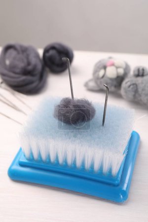 Felting tools, wool and toy cat on light wooden table, closeup