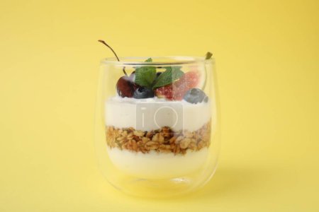 Vidrio con yogur, bayas y granola sobre fondo amarillo