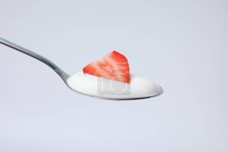 Delicioso yogur natural con fresa fresca en cuchara sobre fondo claro