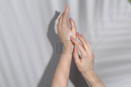 Téléchargez les photos : Femme appliquant de la crème sur sa main sur fond gris, gros plan - en image libre de droit