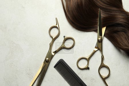 Professionelle Friseurschere und Kamm mit brauner Haarsträhne auf grauem Tisch, flach gelegt