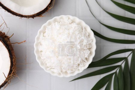 Photo for Coconut flakes in bowl, nuts and palm leaf on white tiled table, flat lay - Royalty Free Image