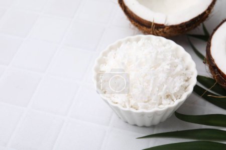 Photo for Coconut flakes in bowl, nuts and palm leaf on white tiled table, space for text - Royalty Free Image
