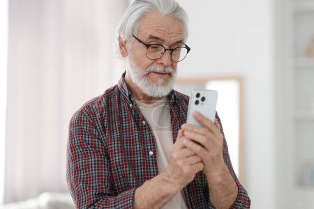Téléchargez les photos : Portrait de grand-père heureux avec des lunettes en utilisant smartphone à l'intérieur - en image libre de droit