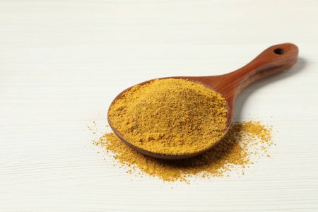Curry powder in spoon on white wooden table. Space for text