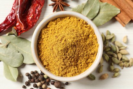 Curry powder in bowl and other spices on white wooden table, flat lay