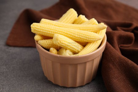 Tasty fresh yellow baby corns in bowl on brown table, closeup