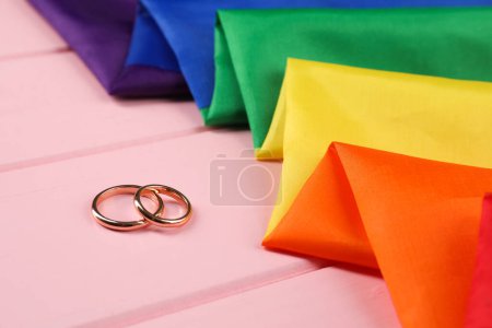 Drapeau LGBT arc-en-ciel et alliances sur table en bois rose, gros plan