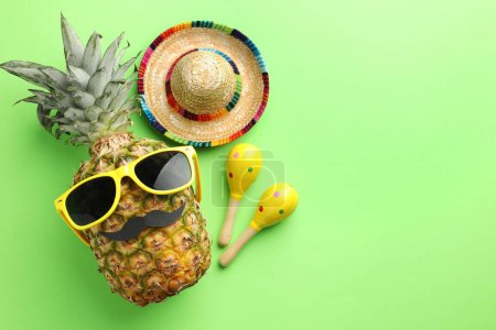 Téléchargez les photos : Chapeau sombrero mexicain, ananas avec lunettes de soleil, fausse moustache et maracas sur fond vert, plat. Espace pour le texte - en image libre de droit