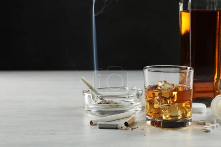 Alcohol y drogadicción. Whisky en vidrio, botella, cigarrillos y pastillas en la mesa blanca, espacio para el texto