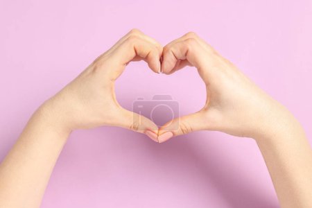 Frau zeigt Herz-Geste mit Händen auf rosa Hintergrund, Nahaufnahme