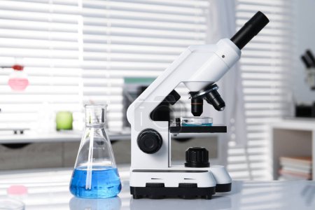 Téléchargez les photos : Analyse de laboratoire. Flacon avec liquide bleu et microscope sur table blanche à l'intérieur - en image libre de droit