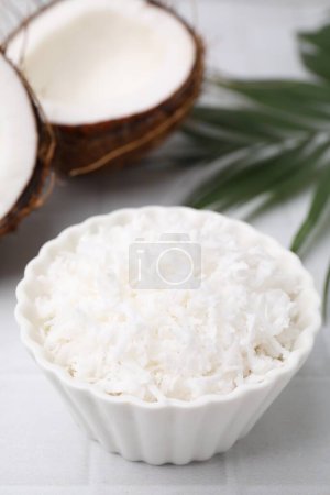 Copos de coco en tazón, nueces y hojas de palma sobre mesa blanca, primer plano