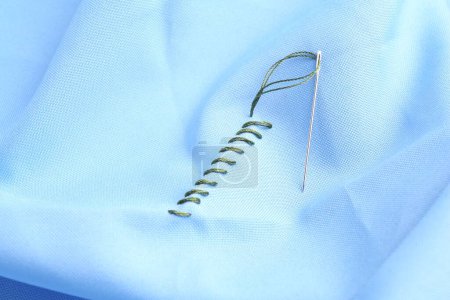 Sewing needle with thread and stitches on light blue cloth, closeup