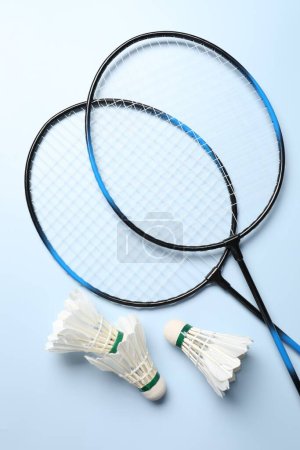 Photo for Feather badminton shuttlecocks and rackets on light blue background, flat lay - Royalty Free Image