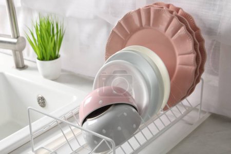 Drainer with different clean dishware on white table in kitchen