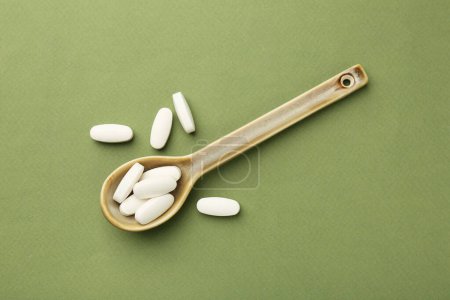 Téléchargez les photos : Pilules de vitamine dans la cuillère sur fond olive, vue de dessus - en image libre de droit