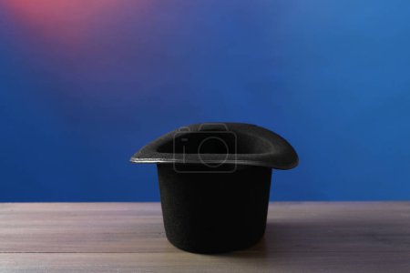 Magician's hat on wooden table against color background