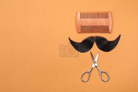 Téléchargez les photos : Moustache artificielle, peigne et ciseaux sur fond orange, vue de dessus. Espace pour le texte - en image libre de droit