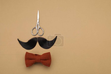 Téléchargez les photos : Moustache artificielle, noeud papillon et ciseaux sur fond beige, vue de dessus. Espace pour le texte - en image libre de droit