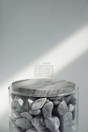 Téléchargez les photos : Présentation du produit. Conteneur en verre avec pierres sur fond gris clair. Espace pour le texte - en image libre de droit