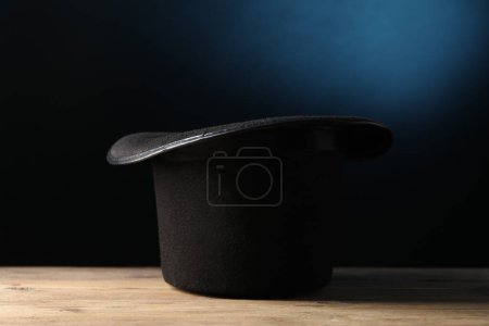 Magician's hat on wooden table against dark background