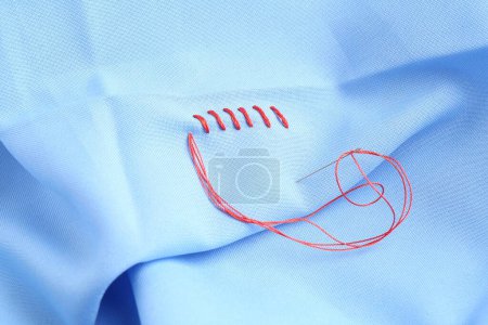 Téléchargez les photos : Aiguille à coudre avec fil et points de suture sur tissu bleu clair, gros plan - en image libre de droit