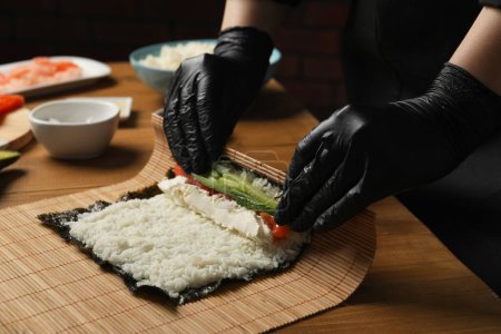 Téléchargez les photos : Chef en gants faisant rouler des sushis à table en bois, gros plan - en image libre de droit