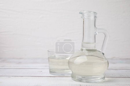 Foto de Vinagre en jarra de vidrio y tazón sobre mesa de madera blanca, espacio para texto - Imagen libre de derechos